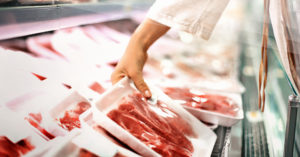 someone picking up red meat from an open case door